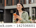 Young woman making video blog walking in city street while smiling and waving to smartphone camera 142506601