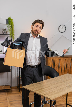 Middle-aged businessman packs personal items in box looks around room with gentle nostalgia softly Middle-aged businessman packs personal items in box looks around room with gentle nostalgia softly 142506602