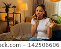 African American young woman on home sofa calling bank support to explain bank card payment problem 142506606