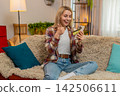 Adult woman checking credit card balance on smartphone at home, surprised by unexpected money bonus 142506611
