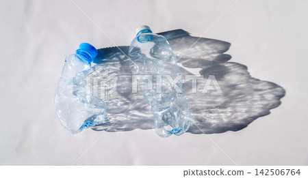 Two empty plastic water bottles on white surface with shadows Two empty plastic water bottles on white surface with shadows 142506764