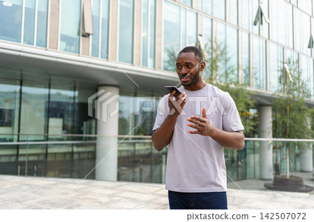 African american man talking on smartphone on street in city outdoor. Man with cell phone chatting with friends. Smiling person making answering call by cellphone. Guy having conversation by mobile African american man talking on smartphone on street in city outdoor. Man with cell phone chatting with friends. Smiling person making answering call by cellphone. Guy having conversation by mobile 142507072
