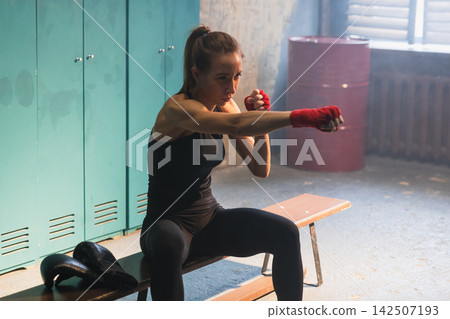 Women self defense girl power. Strong woman fighter punching with red boxing wraps sports protective bandages. Girl punching training punches looking concentrated straight. Fit body workout Women self defense girl power. Strong woman fighter punching with red boxing wraps sports protective bandages. Girl punching training punches looking concentrated straight. Fit body workout 142507193