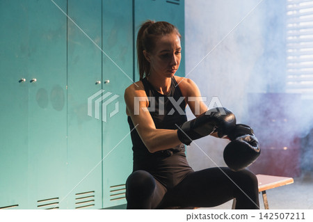 Women self defense girl power. Woman fighter preparing for fight puts on boxing gloves in locker room. Strong girl training punches ready for fight active exercise sparring workout training in gym Women self defense girl power. Woman fighter preparing for fight puts on boxing gloves in locker room. Strong girl training punches ready for fight active exercise sparring workout training in gym 142507211