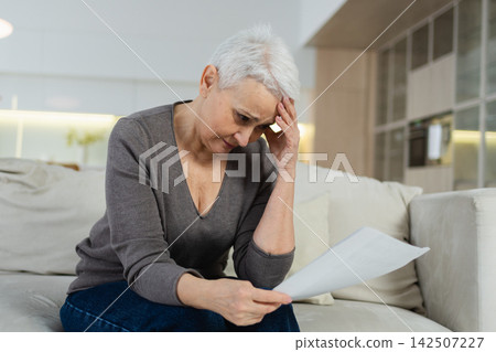 Sad tired ill sick lonely disappointed older senior woman reading bad news at home alone. Unhappy mature grandmother experiencing grief relative death. Stressed elder lady with paper document bill Sad tired ill sick lonely disappointed older senior woman reading bad news at home alone. Unhappy mature grandmother experiencing grief relative death. Stressed elder lady with paper document bill 142507227