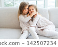 Happy family sisterly love. Two funny little twin sisters girls hugging with love care playing together at home indoors. Happy children lifestyle. Identical twin girls hugs. Girls friendship and youth 142507234