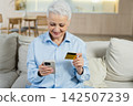 Senior woman shopping online with smartphone paying with credit card at home Old lady buying on Internet enter credit card details Online shopping delivery service. Older generation modern tech usage 142507239