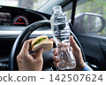Asian lady holding water bottle and bread bakery food in car dangerous and risk an accident. 142507624