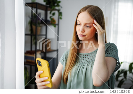 Young woman suffering headache while using smartphone Young woman suffering headache while using smartphone 142510268