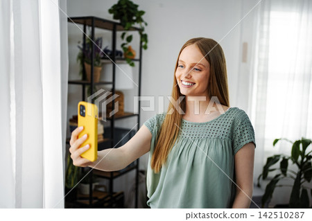 Young woman smiling doing selfie or video call at home 142510287