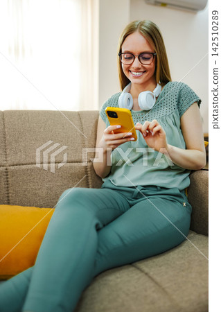 Young woman smiling using smartphone on couch Young woman smiling using smartphone on couch 142510289