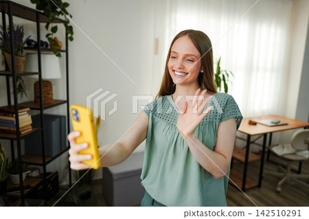 Woman waving during video call using smartphone Woman waving during video call using smartphone 142510291