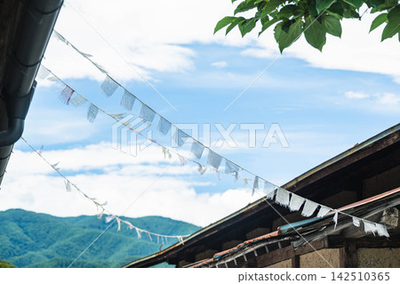 Prayer flags fluttering against a backdrop of blue sky and gentle mountain ranges, and the eaves of an old house. Prayer flags fluttering against a backdrop of blue sky and gentle mountain ranges, and the eaves of an old house. 142510365