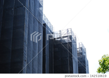 Building under construction, scaffolding, and protective sheeting. Building under construction, scaffolding, and protective sheeting. 142510619
