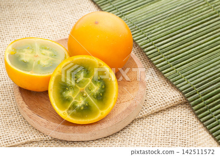 Fruits and slices of lulo or naranjilla on the wooden table - Solanum quitoense Fruits and slices of lulo or naranjilla on the wooden table - Solanum quitoense 142511572