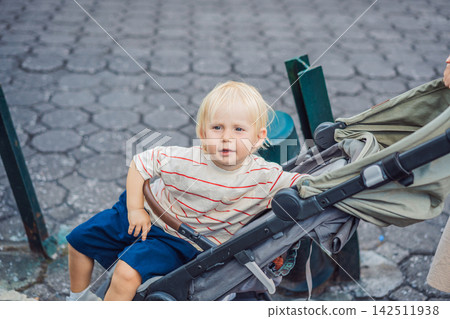 Little blond boy sitting in a stroller on a cobblestone street in Puebla Mexico with urban family travel setting childhood portrait historic pavement and relaxed city vacation atmosphere. 142511938