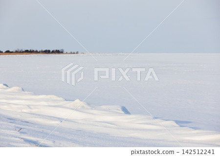 Snow-covered frozen lake with gentle snowdrifts along a quiet shoreline Snow-covered frozen lake with gentle snowdrifts along a quiet shoreline 142512241