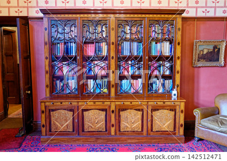 Study interior with a large wood marquetry bookcase, leather armchairs, and stenciled wallpaper borders at Knightshayes Court Study interior with a large wood marquetry bookcase, leather armchairs, and stenciled wallpaper borders at Knightshayes Court 142512471