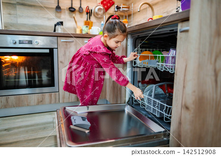 Little girl emptying the dishwasher in a modern kitchen Little girl emptying the dishwasher in a modern kitchen 142512908
