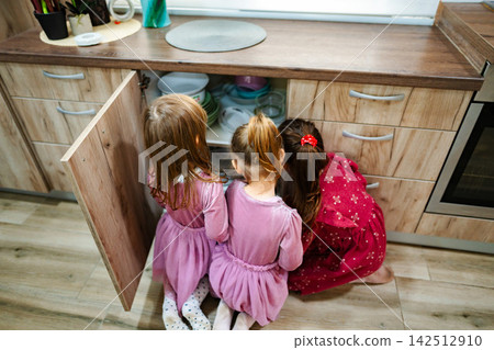 Three little girls exploring kitchen cabinets looking for sweets and snacks Three little girls exploring kitchen cabinets looking for sweets and snacks 142512910