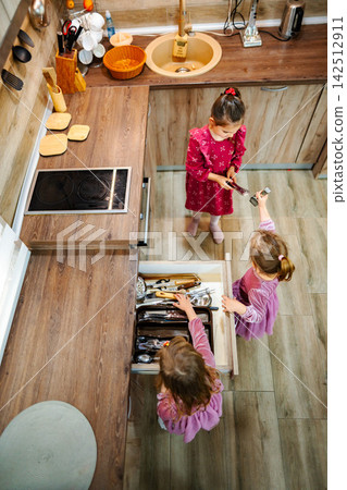 Three little girls playing with kitchen utensils in a modern kitchen Three little girls playing with kitchen utensils in a modern kitchen 142512911