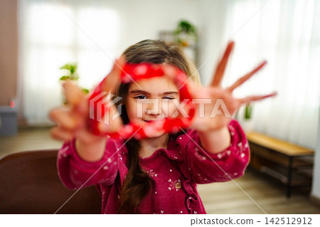 Little girl winking and making a heart shape with her hands 142512912