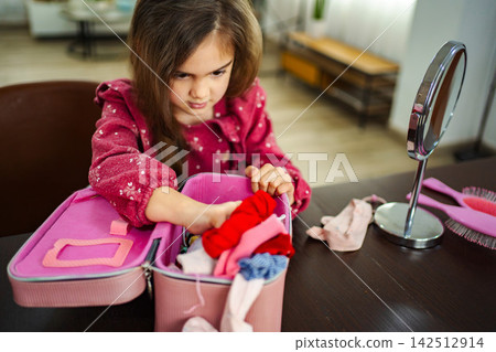 Little girl playing with doll clothes and accessories at home Little girl playing with doll clothes and accessories at home 142512914