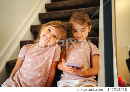 Little sisters bonding on stairs using smartphone Little sisters bonding on stairs using smartphone 142512916