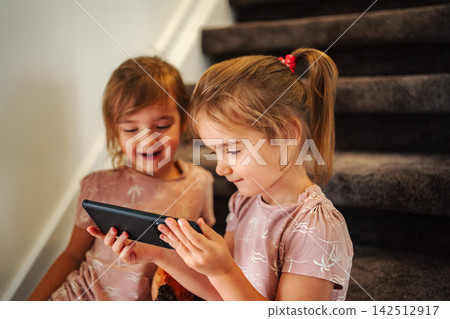 Young sisters sharing a smartphone screen watching digital content Young sisters sharing a smartphone screen watching digital content 142512917