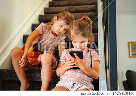 Young sisters sitting on stairs watching smartphone screen Young sisters sitting on stairs watching smartphone screen 142512919