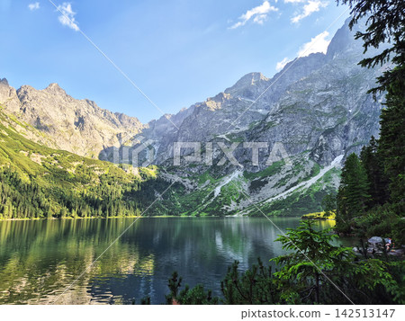 Scenic High Tatra mountains with a small forest lake beneath rugged rocky summits. Natural wilderness landscape between Poland and Slovakia. Scenic High Tatra mountains with a small forest lake beneath rugged rocky summits. Natural wilderness landscape between Poland and Slovakia. 142513147