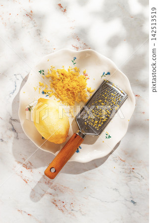 Lemon zest and peeler on a plate with floral design in a bright kitchen Lemon zest and peeler on a plate with floral design in a bright kitchen 142513519