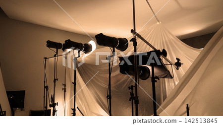 Shooting studio for photographer and creative art director with production setting up lighting flash and LED headlight on tripod and professional equipment for portrait model or product photo shoot. Shooting studio for photographer and creative art director with production setting up lighting flash and LED headlight on tripod and professional equipment for portrait model or product photo shoot. 142513845