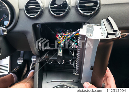 Hand holding car stereo amplifier with wires from dashboard installation slot. Concept of car audio upgrade, auto electronics repair, vehicle installation, car service Hand holding car stereo amplifier with wires from dashboard installation slot. Concept of car audio upgrade, auto electronics repair, vehicle installation, car service 142513904