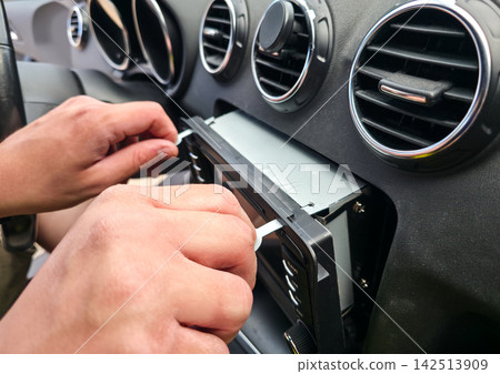 Hands using removal keys to pull car stereo from dashboard panel. Concept of car audio upgrade, auto electronics repair, vehicle installation, car service 142513909