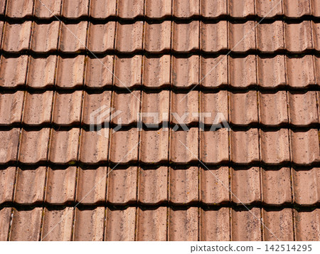 Close-up of a traditional terracotta tiled roof, showing weathered roofing materials, repeating patterns and architectural details. Close-up of a traditional terracotta tiled roof, showing weathered roofing materials, repeating patterns and architectural details. 142514295