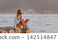 Woman Sitting on Stone Pier Reading Book 142514847