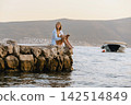 Woman Reading Paper Book on Stone Pier with Boat 142514849