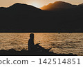 Woman Reading Paper Book on Pier by Sea at Sunset 142514851