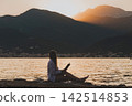 Woman Reading Paper Book on Sea Shore at Sunset 142514853