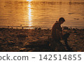 Man Playing Acoustic Guitar on River Bank at Sunset 142514855