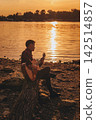 Musician Playing Acoustic Guitar on River Shore 142514857