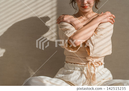 A woman in her 40s performs self-care with her hand on her shoulder; the interplay of light and shadow creates a striking image of beauty and health. A woman in her 40s performs self-care with her hand on her shoulder; the interplay of light and shadow creates a striking image of beauty and health. 142515235