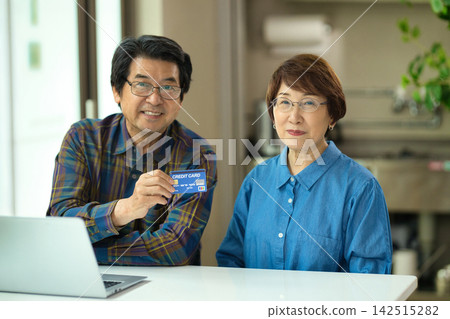 一對老年夫婦一邊看著電腦一邊輸入信用卡資訊。 一對老年夫婦一邊看著電腦一邊輸入信用卡資訊。 142515282