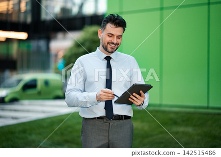 Businessman smiling while working on digital tablet outdoors Businessman smiling while working on digital tablet outdoors 142515486