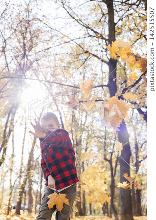 Boy in red plaid shirt standing in autumn forest with sun flare Boy in red plaid shirt standing in autumn forest with sun flare 142515507