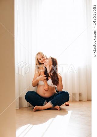 A pregnant woman with her daughter in a cozy home atmosphere. Waiting for a child in the family. Portrait of mother and daughter A pregnant woman with her daughter in a cozy home atmosphere. Waiting for a child in the family. Portrait of mother and daughter 142515582