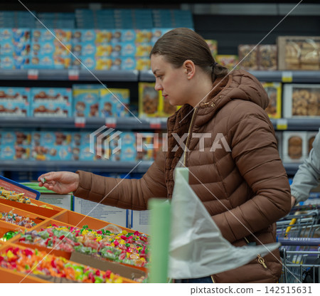 Girl choosing candy. Shopper excitedly chooses bright candies amid sale and weekend shopping vibe. Woman eagerly grabs assorted sweets from display with bright lighting during lively shopping trip Girl choosing candy. Shopper excitedly chooses bright candies amid sale and weekend shopping vibe. Woman eagerly grabs assorted sweets from display with bright lighting during lively shopping trip 142515631