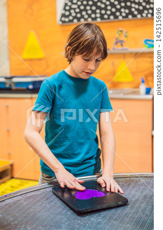 Boy experimenting with hands on science activity in a learning space indoors with interactive equipment STEM education curiosity creative play concentration and holding food. 142515696