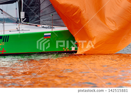 yachtsman assembles a light thin sail spinnaker during sailing regatta in the Gulf of Finland at sunny day, life jacket, board of the sailing boat, teamwork, reflections yachtsman assembles a light thin sail spinnaker during sailing regatta in the Gulf of Finland at sunny day, life jacket, board of the sailing boat, teamwork, reflections 142515881